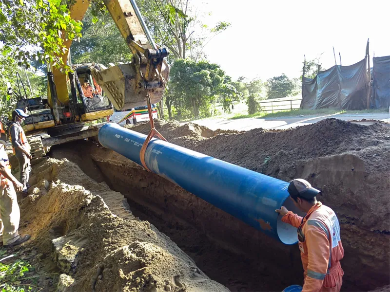 Excavadora bajando tubería de hierro dúctil a la zanja