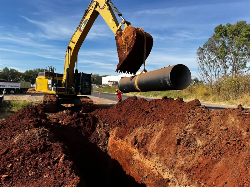 Excavadora colocando tubería de gran diámetro en la zanja