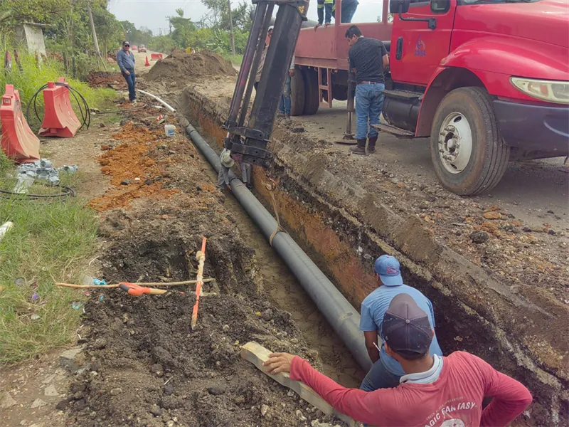 Cuadrilla colocando tubería de 10″ en zanja junto a la carretera